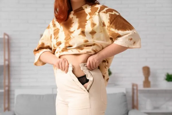 Image of woman trying to do her trousers up after pregnancy weight gain Esher