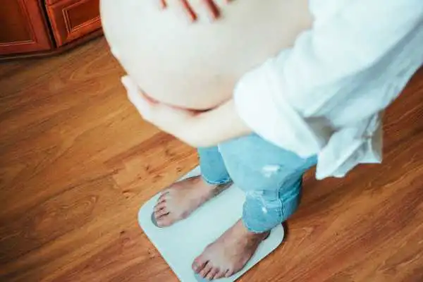 Image of woman weighing herself and experiencing weight gain through pregnancy Esher