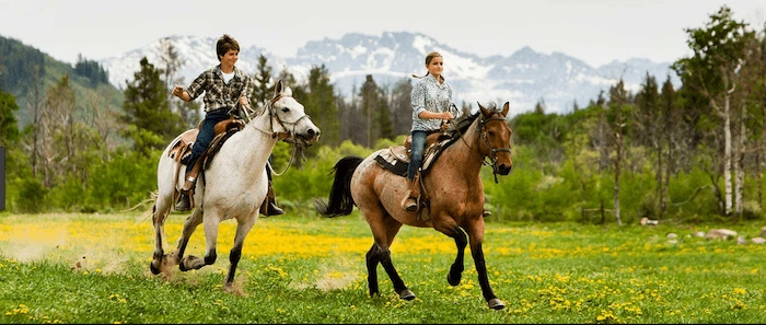 Confident plus-size woman riding Esher a horse through a field with a smile on her face.